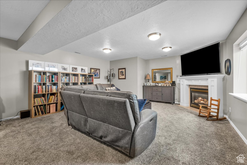 Living room featuring carpet flooring, a glass covered fireplace, a textured ceiling, and baseboards