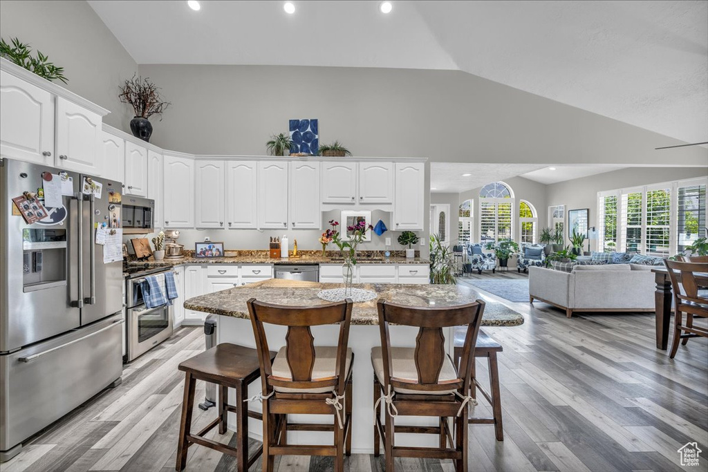 Kitchen featuring stainless steel appliances, open floor plan, high vaulted ceiling, white cabinets, and a breakfast bar area
