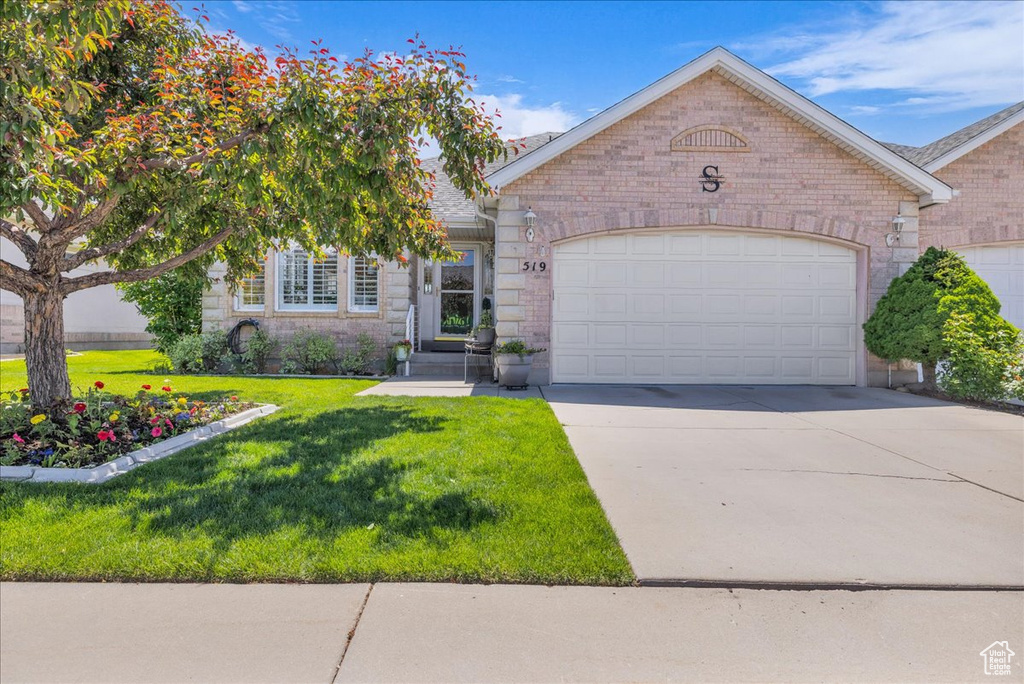 View of front of property with a garage, concrete driveway, a front lawn, and brick siding