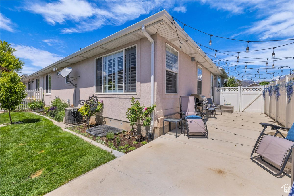 View of side of home featuring stucco siding, a patio area, a gate, and cooling unit
