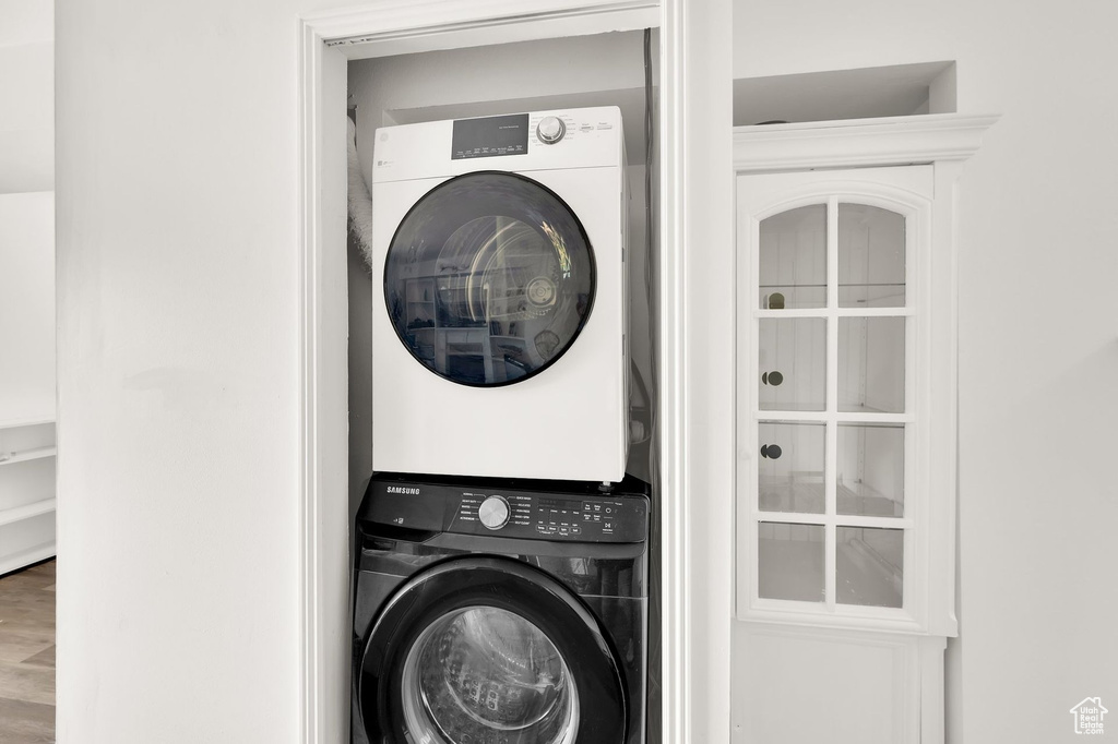 Laundry area with stacked washer / drying machine and wood finished floors
