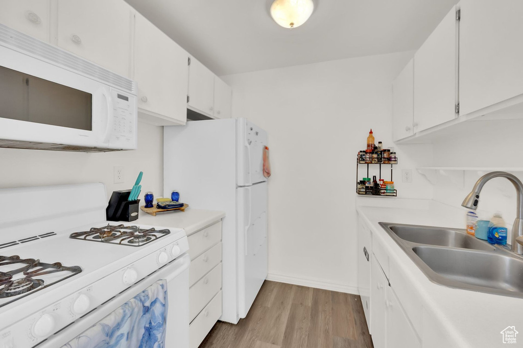 Kitchen featuring white appliances, a sink, wood finished floors, light countertops, and white cabinets