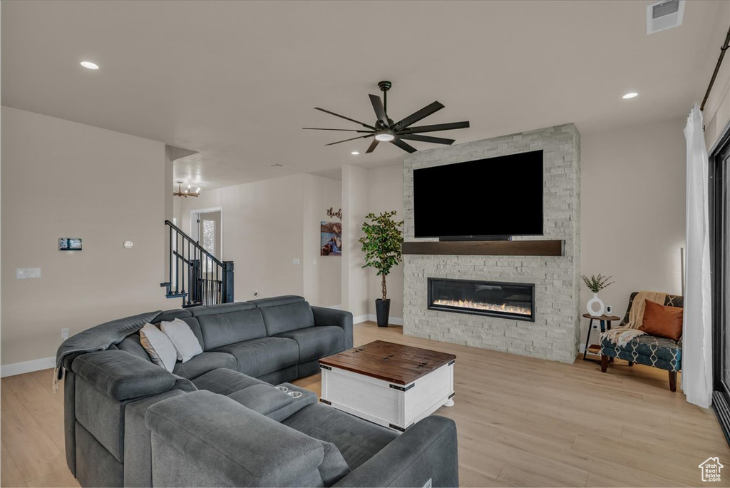 Living room with light wood-type flooring, ceiling fan, a stone fireplace, stairway, and recessed lighting