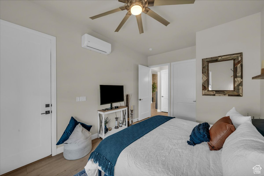 Bedroom with a wall mounted AC, wood finished floors, a ceiling fan, and baseboards