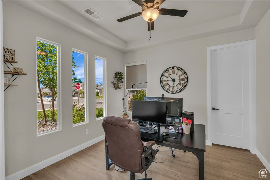 Office space with healthy amount of natural light, a tray ceiling, and wood finished floors