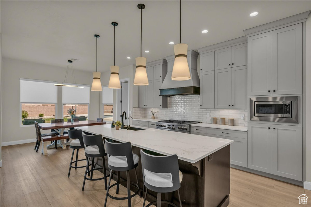 Kitchen featuring custom exhaust hood, backsplash, stainless steel appliances, light wood-style flooring, and baseboards