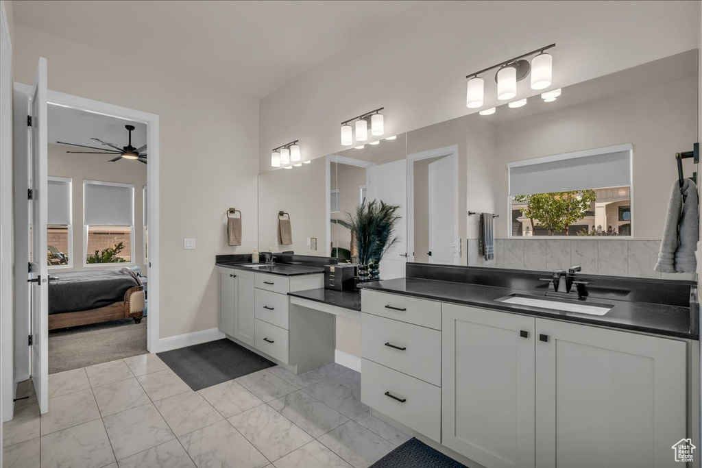 Full bath with marble look tiles, two vanities, ceiling fan, ensuite bath, and baseboards