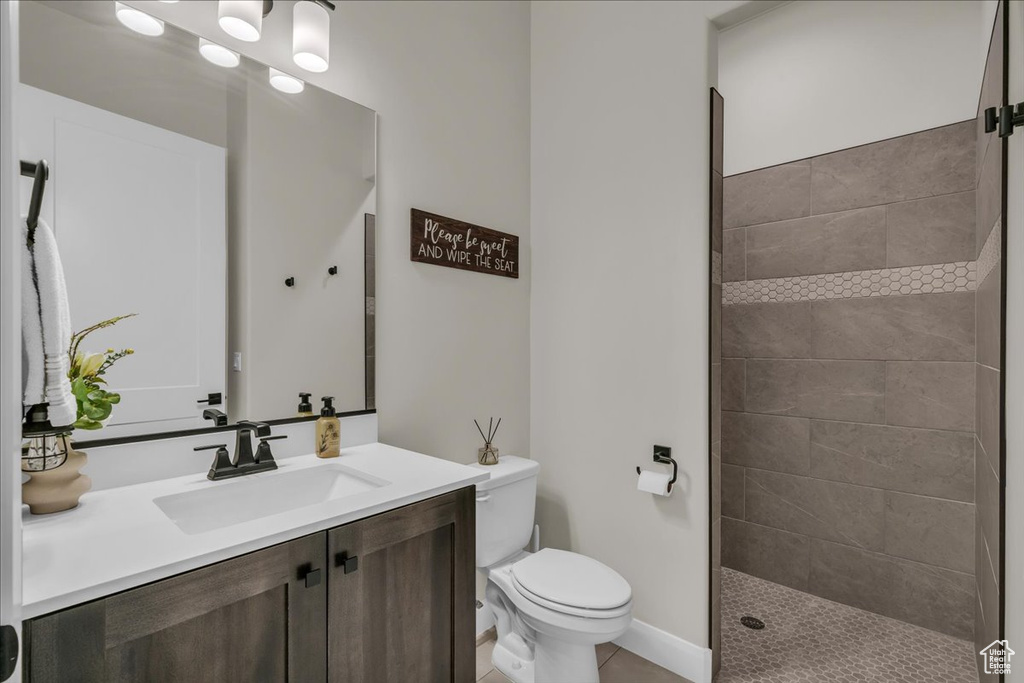 Bathroom featuring toilet, vanity, a tile shower, tile patterned floors, and baseboards