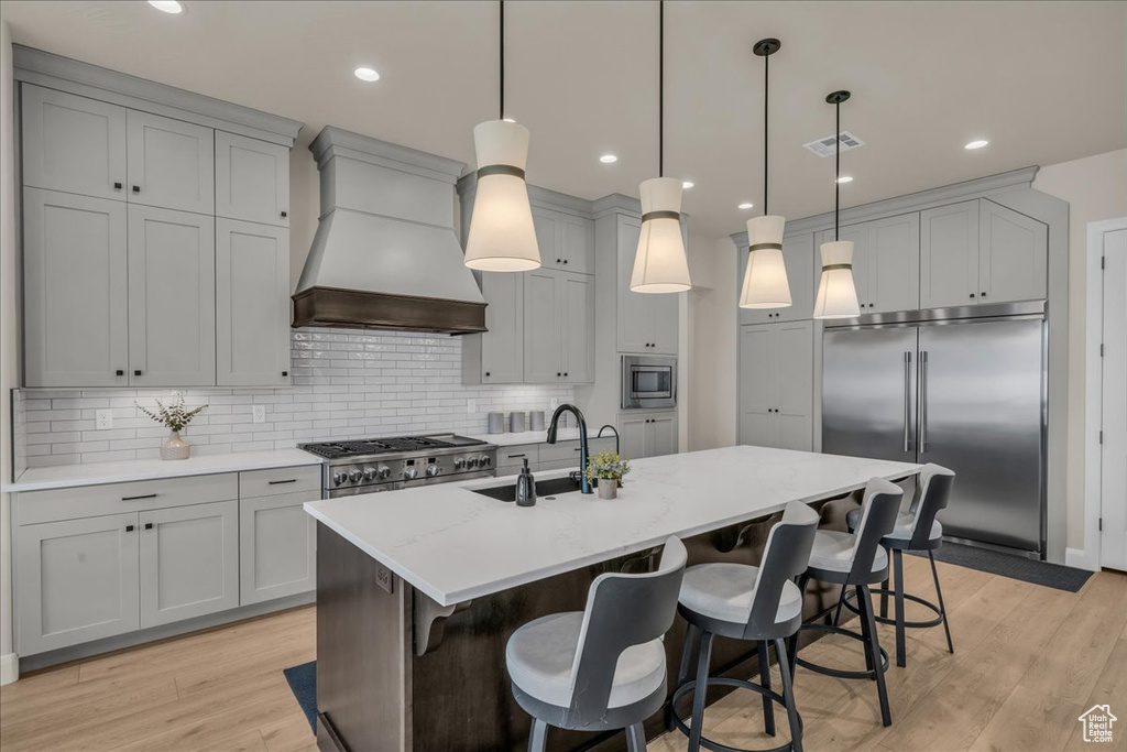 Kitchen featuring built in appliances, premium range hood, a sink, light wood-style floors, and backsplash