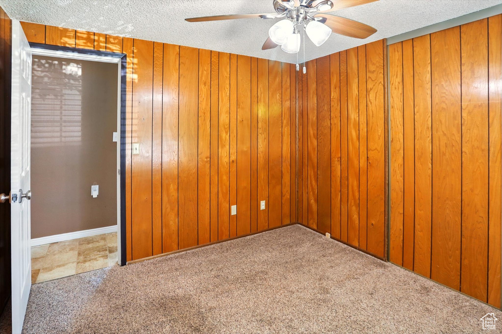 Carpeted spare room with ceiling fan, a textured ceiling, and wooden walls