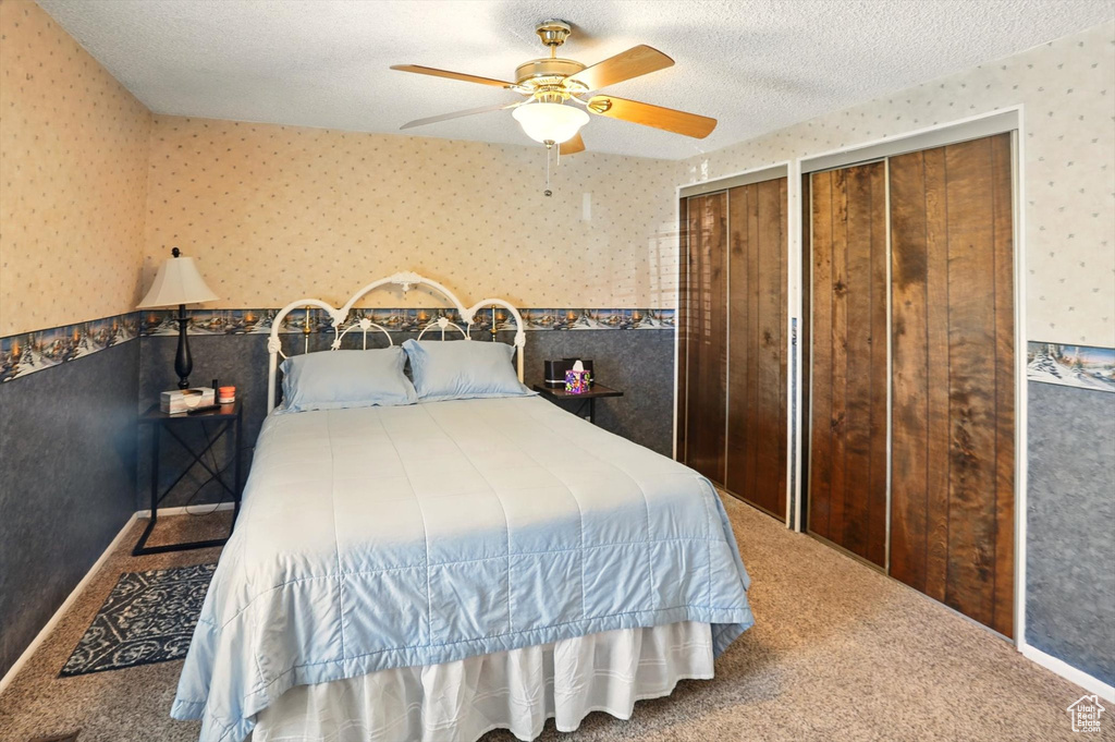 Bedroom with wallpapered walls, two closets, carpet, ceiling fan, and a textured ceiling