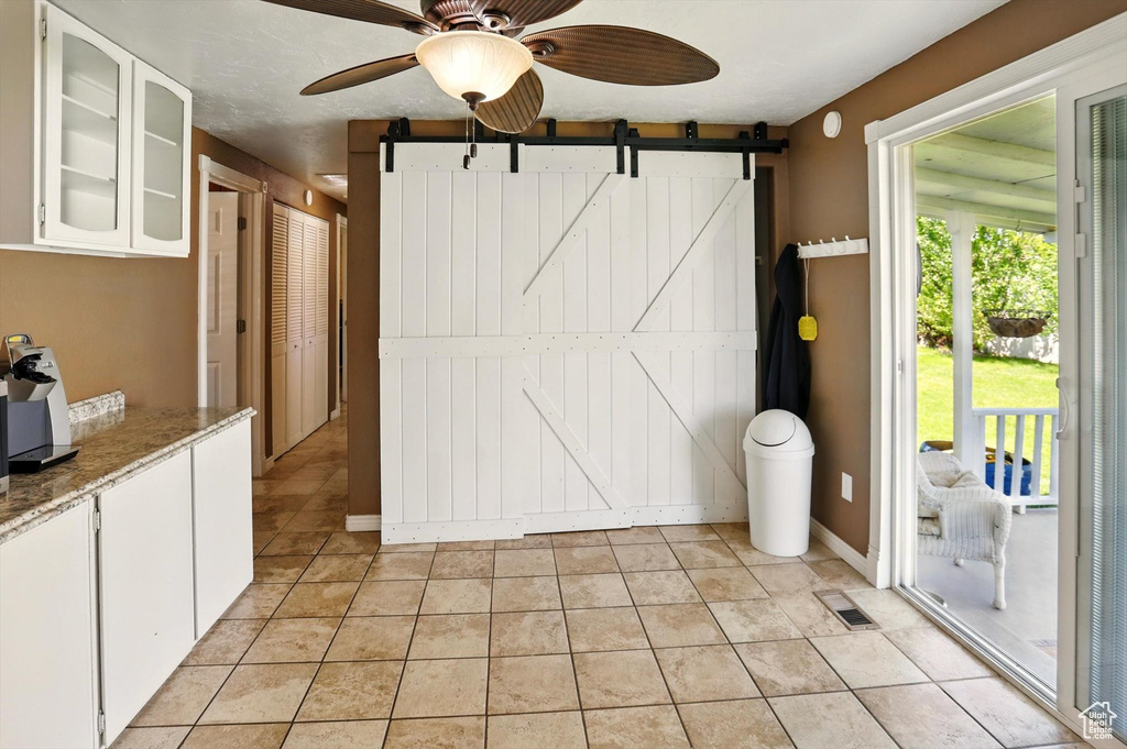 Interior space with ceiling fan, a barn door, light tile patterned flooring, and baseboards