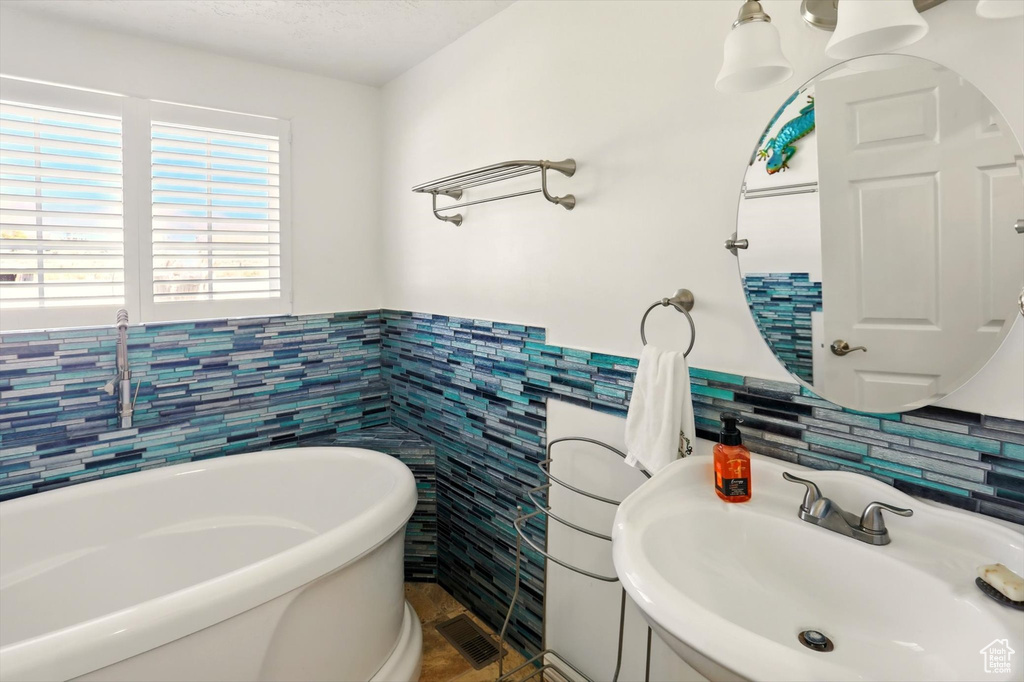 Bathroom featuring tile walls, a sink, a freestanding bath, and wainscoting