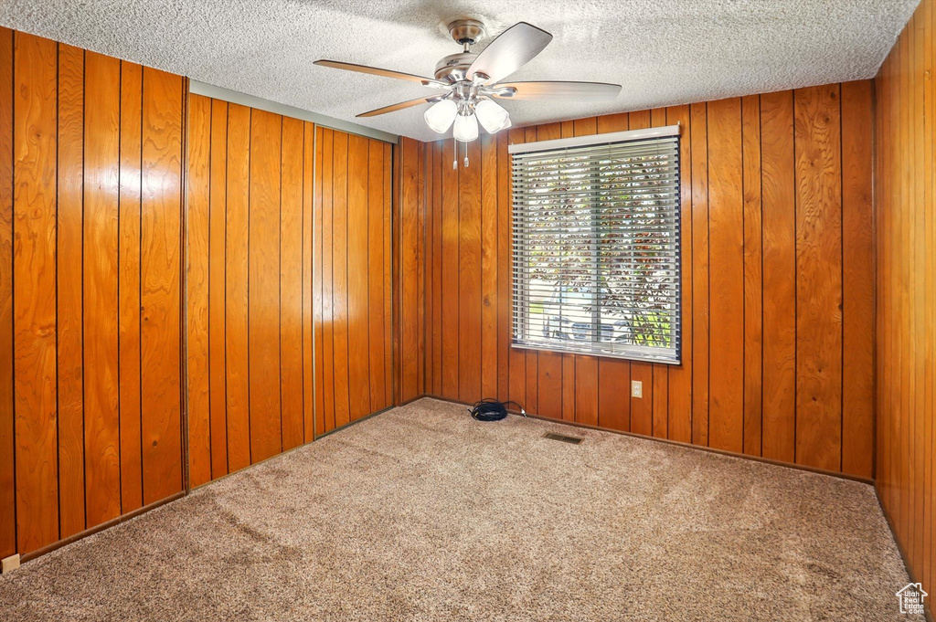 Spare room featuring a ceiling fan, carpet flooring, a textured ceiling, and wooden walls