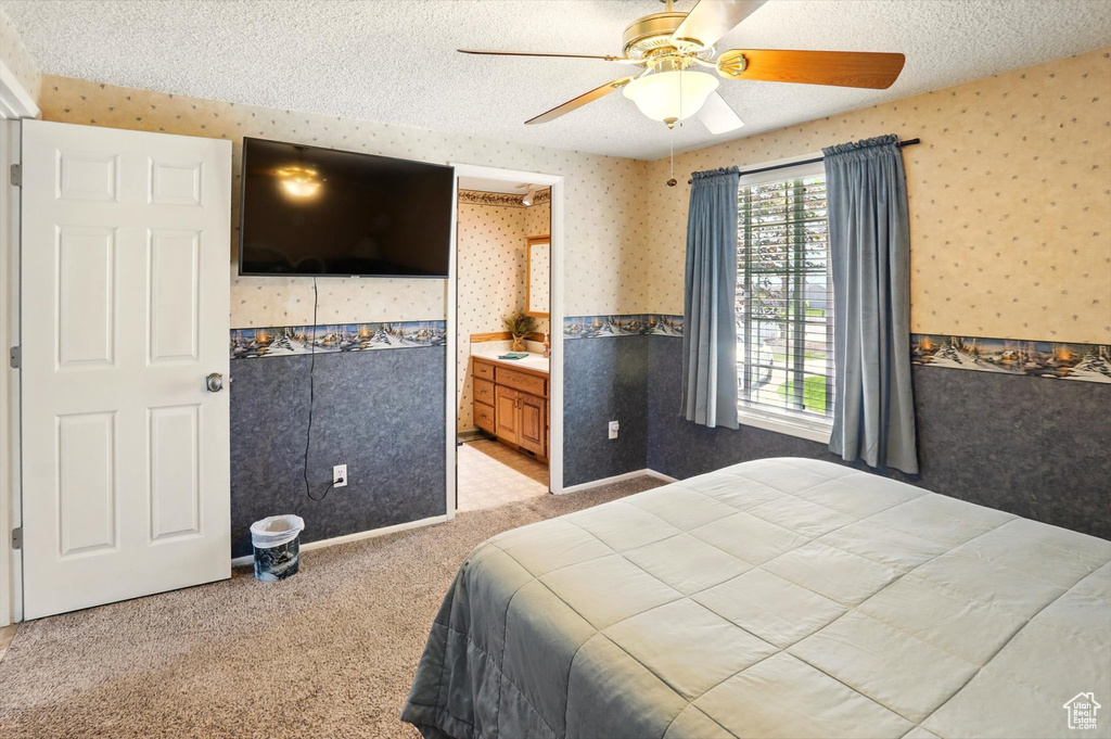 Bedroom with wallpapered walls, a textured ceiling, carpet flooring, a ceiling fan, and connected bathroom