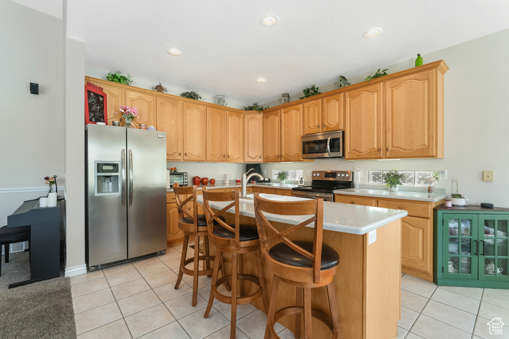Kitchen with appliances with stainless steel finishes, light tile patterned floors, light countertops, a center island with sink, and recessed lighting