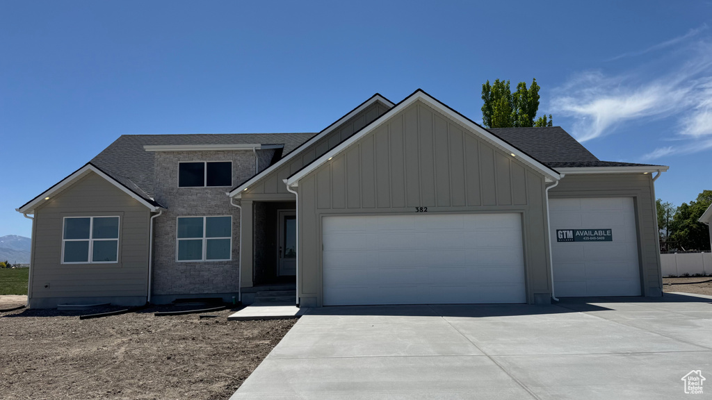 View of front of house with a garage, driveway, board and batten siding, and a shingled roof