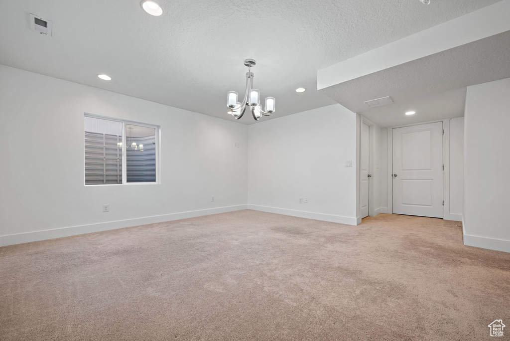 Empty room with a chandelier, baseboards, light colored carpet, recessed lighting, and a textured ceiling