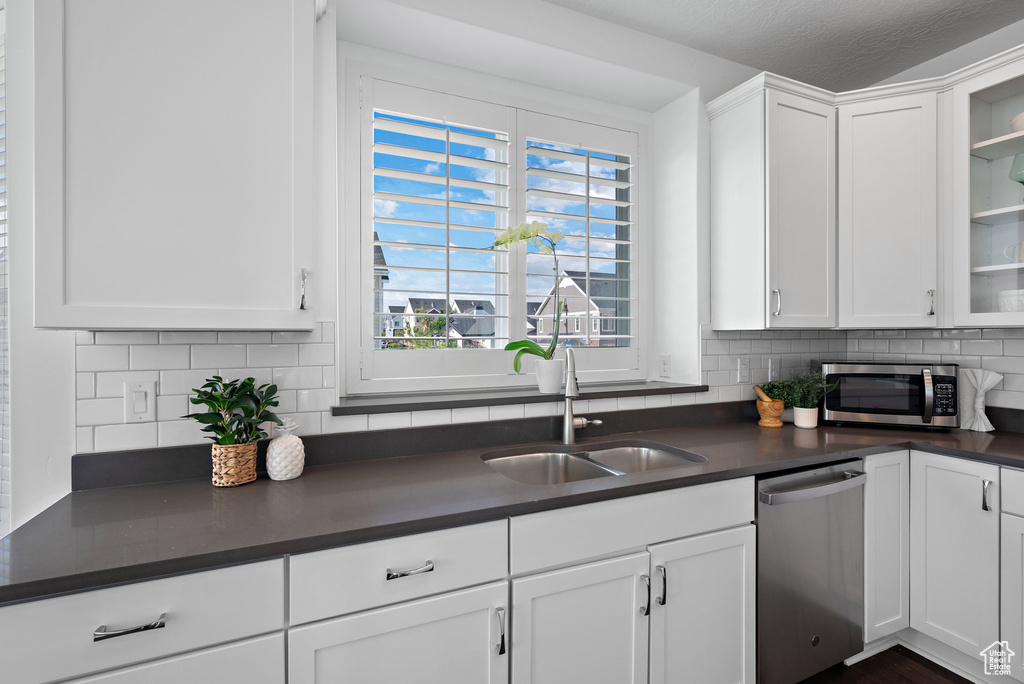Kitchen with appliances with stainless steel finishes, dark countertops, backsplash, and white cabinets