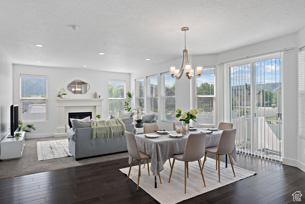 Dining space featuring hardwood / wood-style flooring, a textured ceiling, a chandelier, a fireplace, and recessed lighting