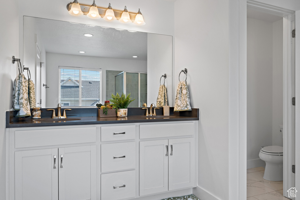Bathroom with marble finish flooring, double vanity, a shower stall, toilet, and baseboards