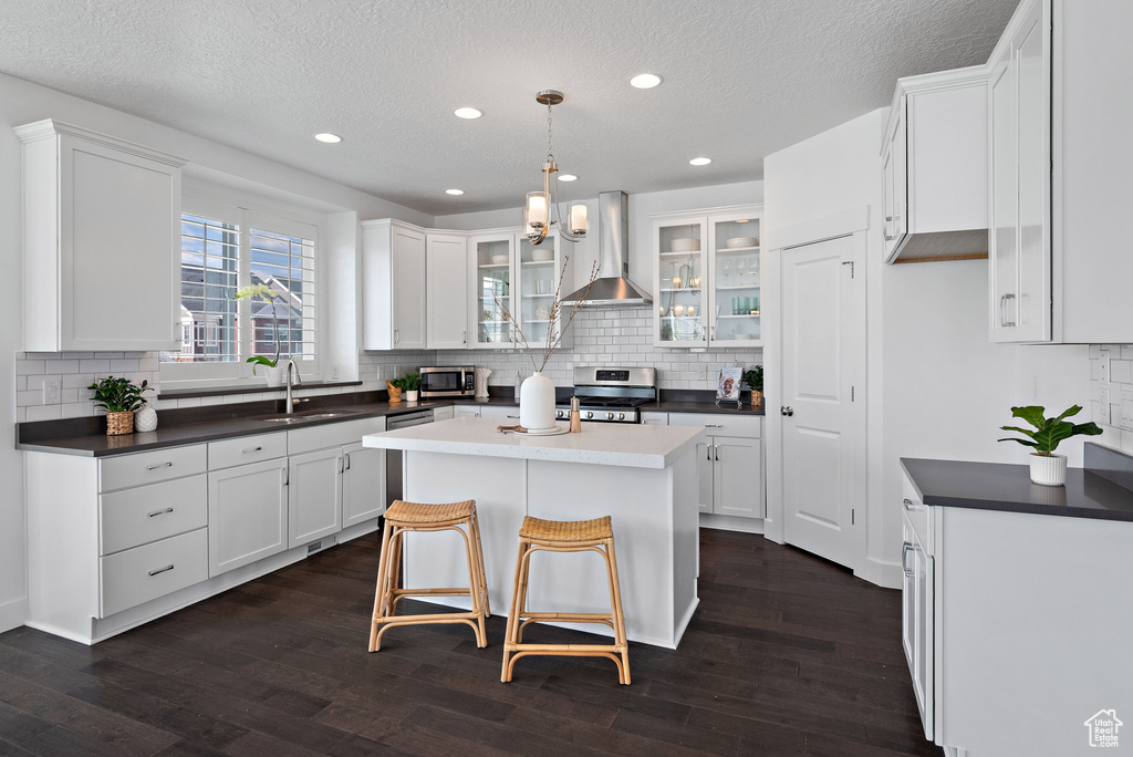 Kitchen featuring wall chimney exhaust hood, appliances with stainless steel finishes, dark countertops, tasteful backsplash, and a textured ceiling