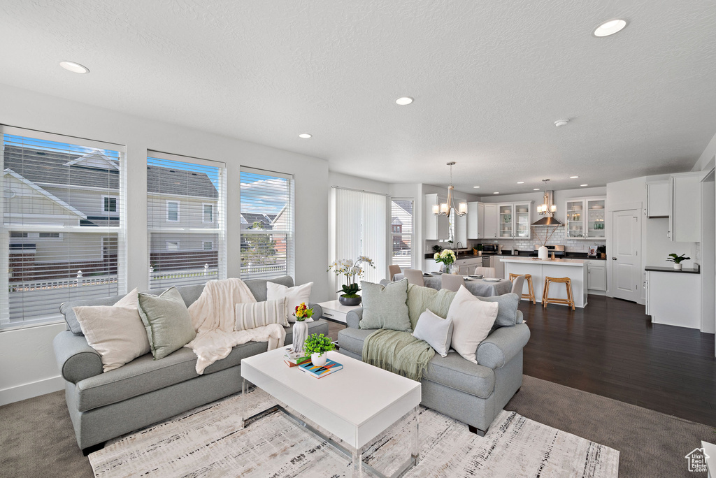 Living area featuring a chandelier, recessed lighting, a textured ceiling, baseboards, and dark colored carpet