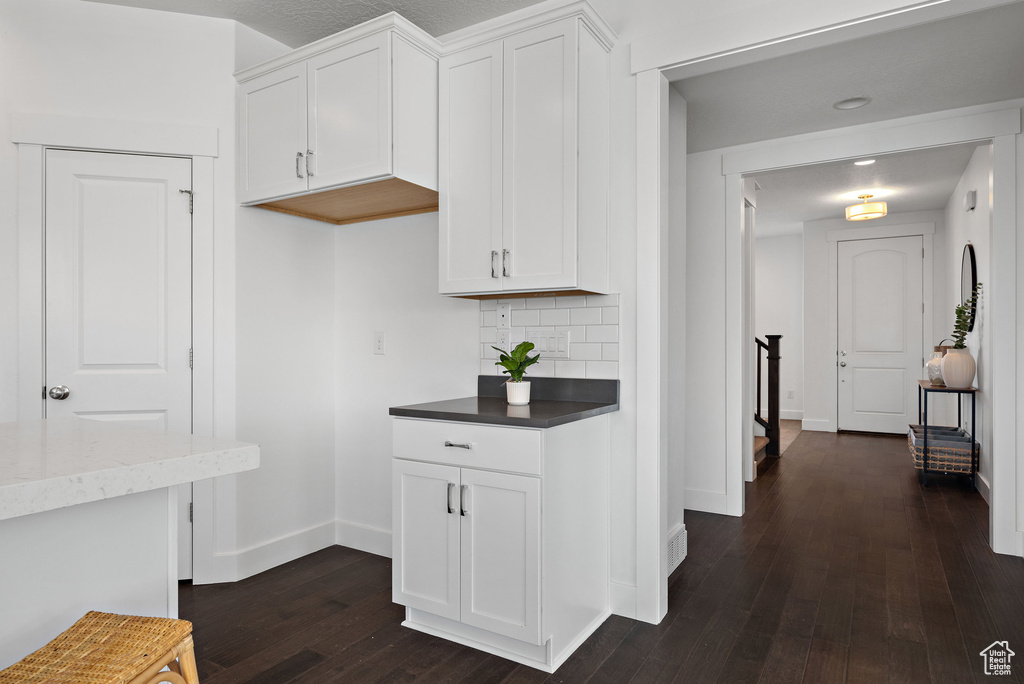 Kitchen with dark wood-style flooring, baseboards, white cabinetry, and tasteful backsplash