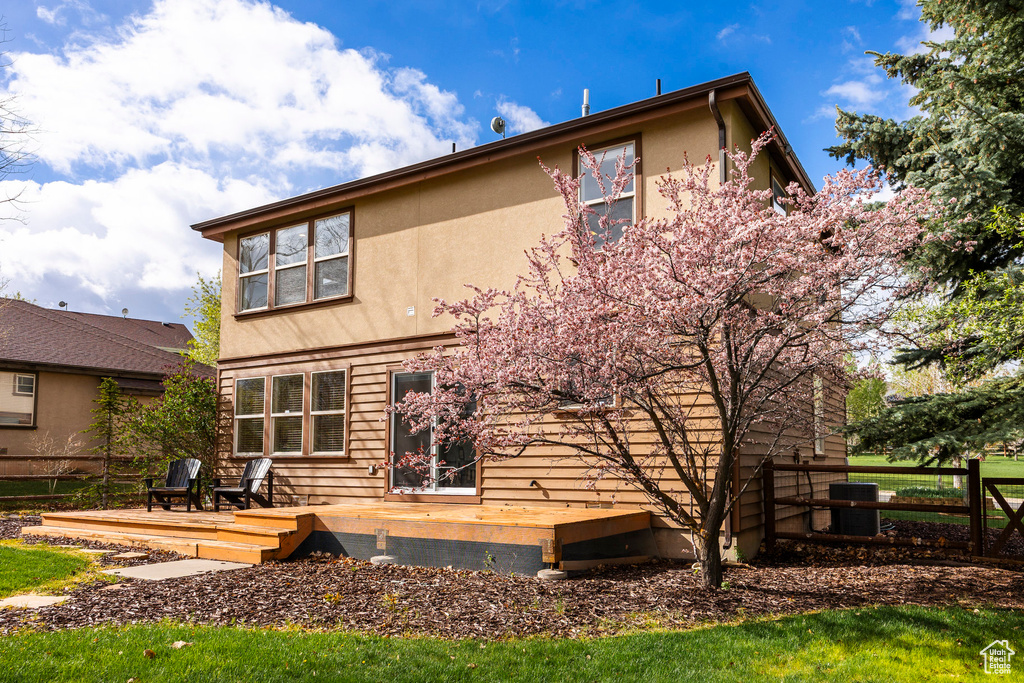 Rear view of house featuring stucco siding, central AC unit, and a deck