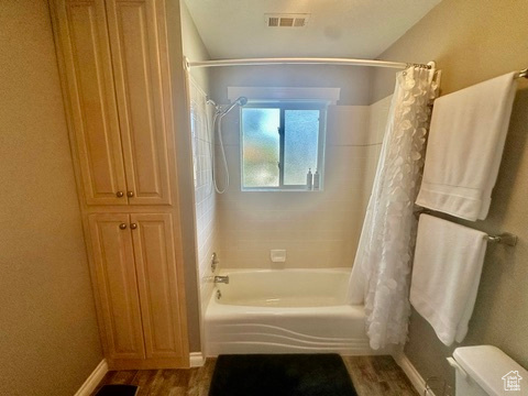Full bath featuring shower / bath combo with shower curtain, toilet, baseboards, and wood finished floors