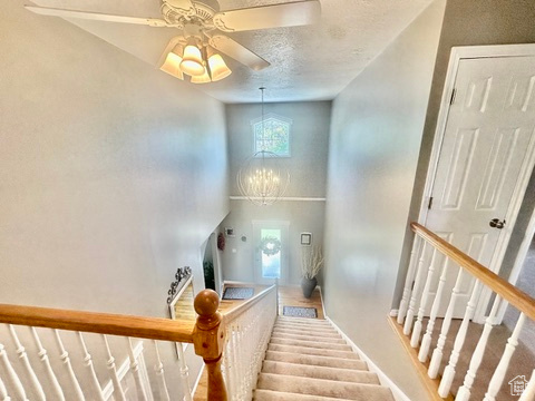 Staircase with a towering ceiling, a textured ceiling, baseboards, ceiling fan, and a chandelier