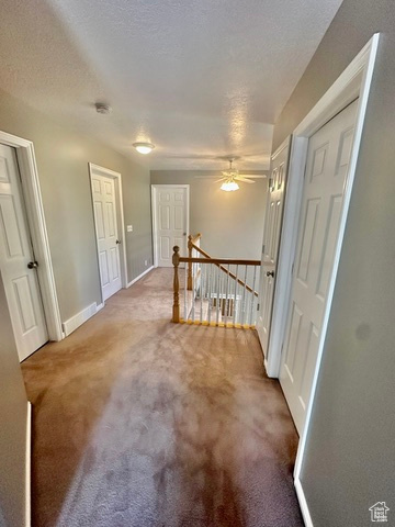 Hallway featuring an upstairs landing, carpet, baseboards, and a textured ceiling