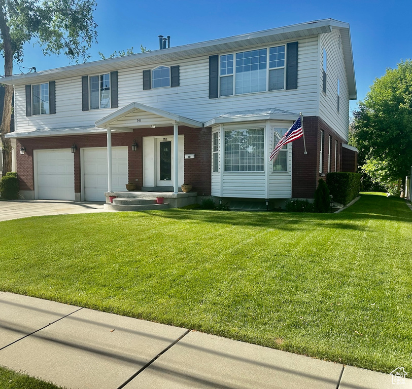 View of front of house featuring brick siding, a garage, driveway, and a front lawn