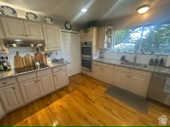 Kitchen with appliances with stainless steel finishes, under cabinet range hood, backsplash, and light wood-style flooring