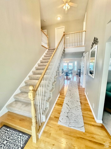 Stairs featuring a towering ceiling, wood finished floors, ceiling fan, and baseboards