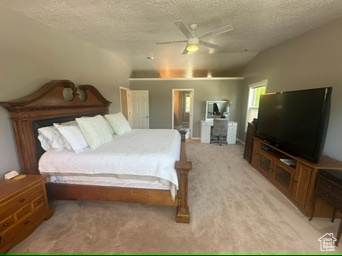Bedroom featuring a textured ceiling, light colored carpet, vaulted ceiling, and ceiling fan