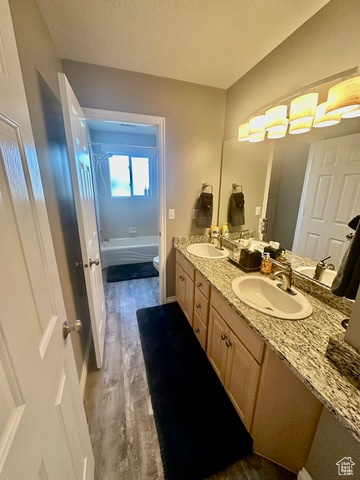 Full bathroom featuring toilet, double vanity, wood finished floors, and tub / shower combination