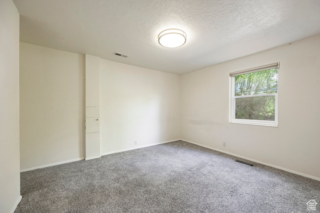 Carpeted spare room with a textured ceiling and baseboards