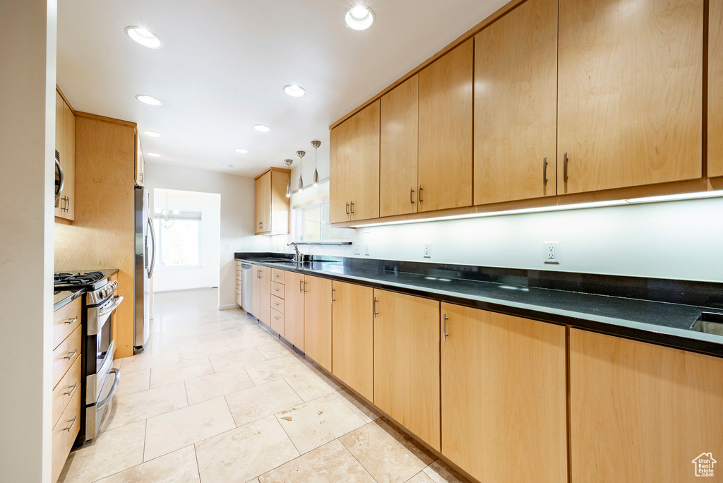 Kitchen with appliances with stainless steel finishes, dark countertops, a sink, light brown cabinetry, and recessed lighting