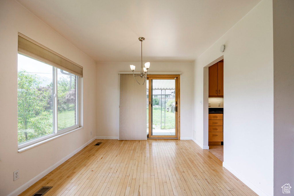 Unfurnished dining area with a chandelier, light wood finished floors, and baseboards