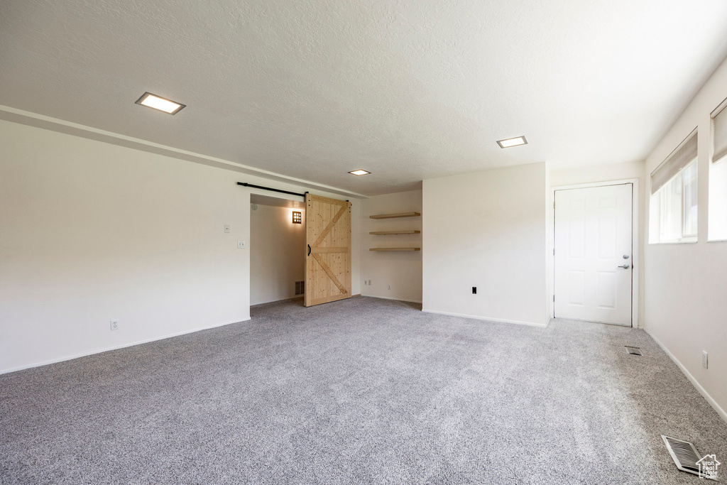 Unfurnished living room with a barn door, light carpet, a textured ceiling, and baseboards