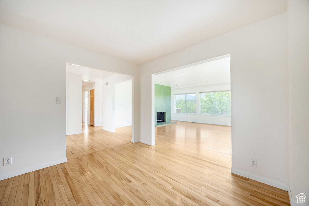 Unfurnished room with light wood-style flooring, a large fireplace, and baseboards
