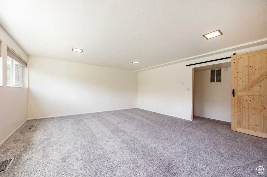 Unfurnished room featuring a barn door, carpet floors, and baseboards