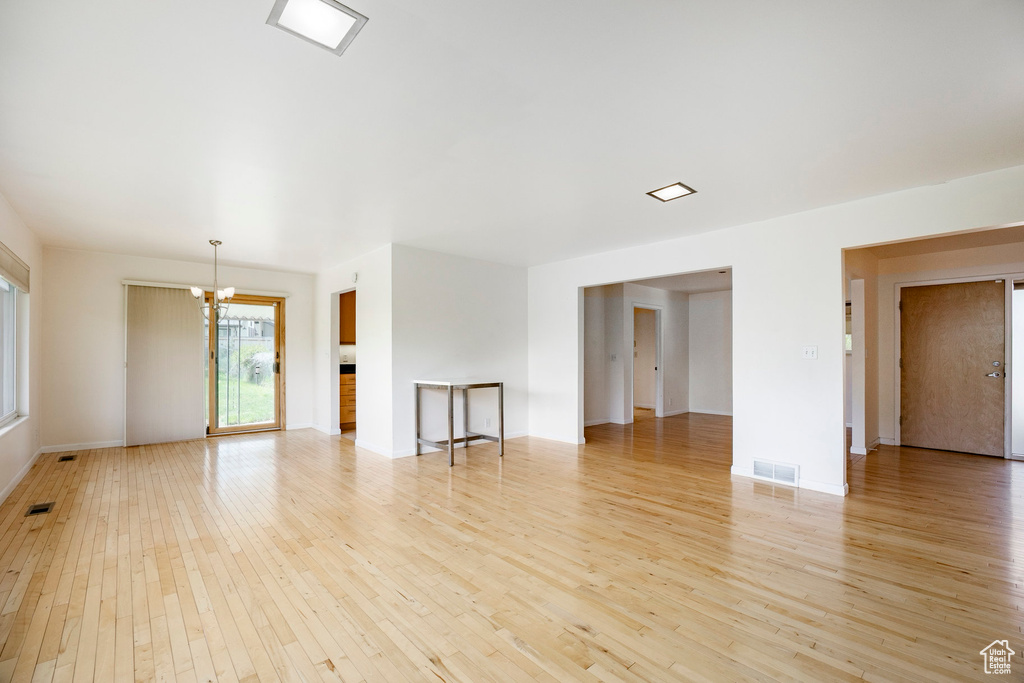 Unfurnished living room with a chandelier, light wood-style flooring, and baseboards