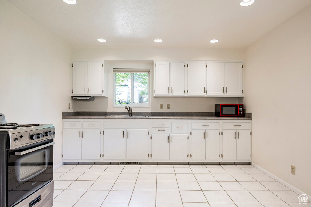 Kitchen with range, a sink, dark countertops, white cabinets, and recessed lighting