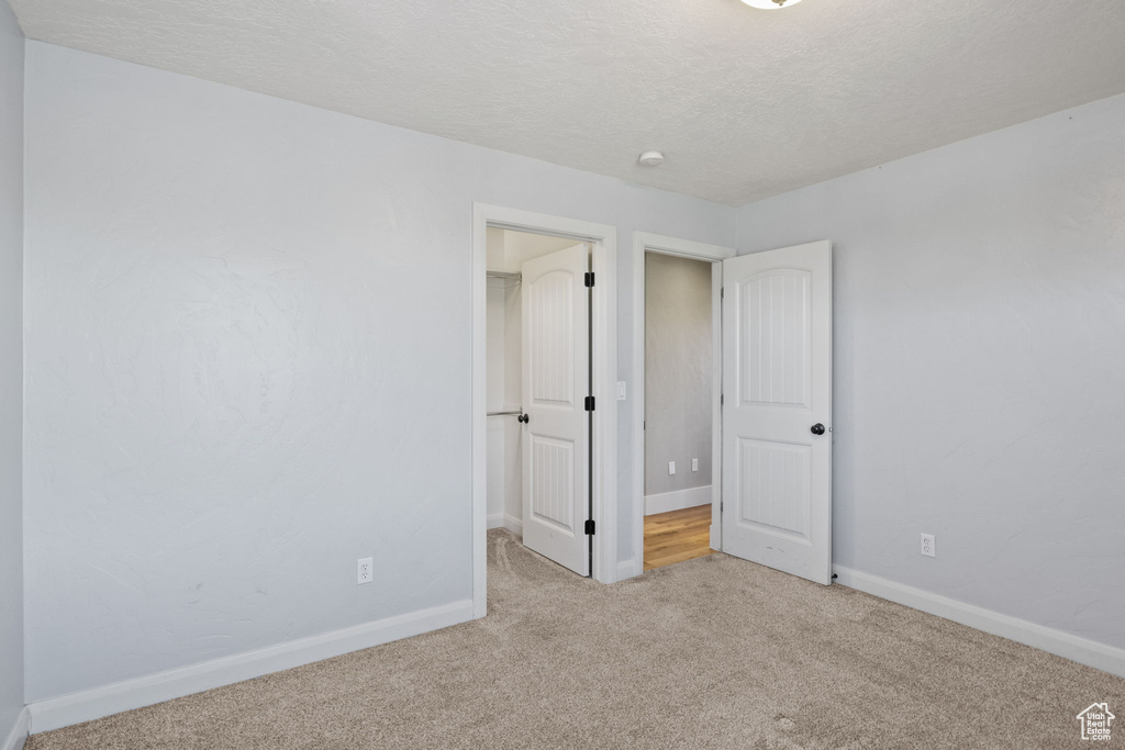 Unfurnished bedroom with carpet floors, a walk in closet, baseboards, a textured ceiling, and a closet