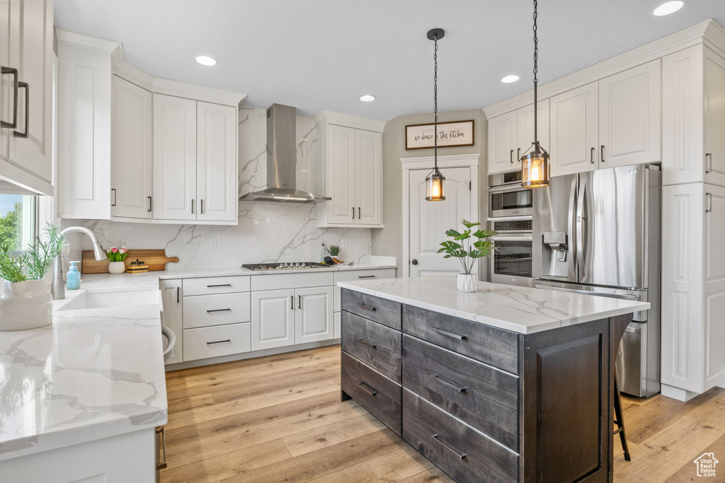 Kitchen featuring stainless steel fridge, wall chimney exhaust hood, a sink, white cabinets, and decorative backsplash