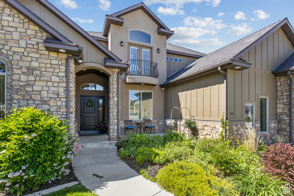 Entrance to property featuring a balcony, stone siding, board and batten siding, and roof with shingles