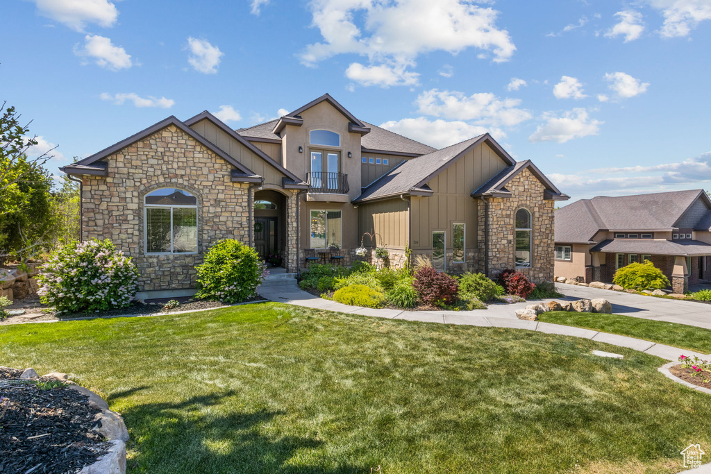 Craftsman house with board and batten siding, stone siding, a front lawn, a balcony, and a shingled roof