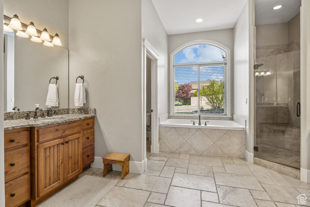 Bathroom with vanity, a garden tub, a stall shower, baseboards, and stone tile flooring